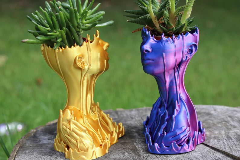 Due vasi artistici a forma di busto, uno dorato e uno blu viola, con piante sulla testa