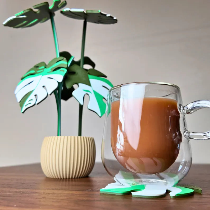 Tazza di caffè in vetro accanto a una pianta decorativa Monstera su tavolo in legno