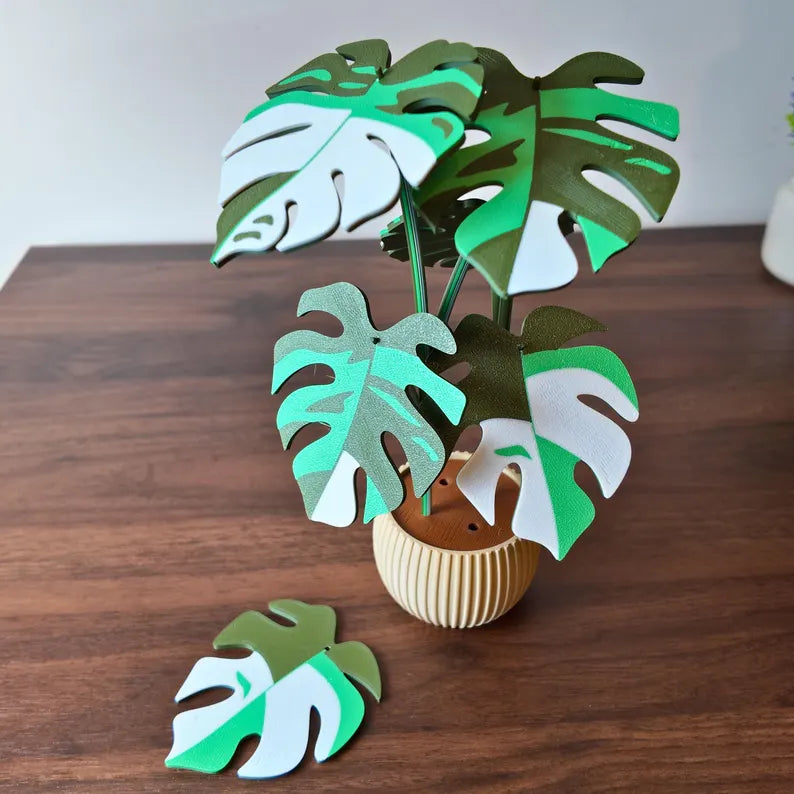 Pianta decorativa stilizzata tipo Monstera in vaso chiaro appoggiata su un tavolo in legno
