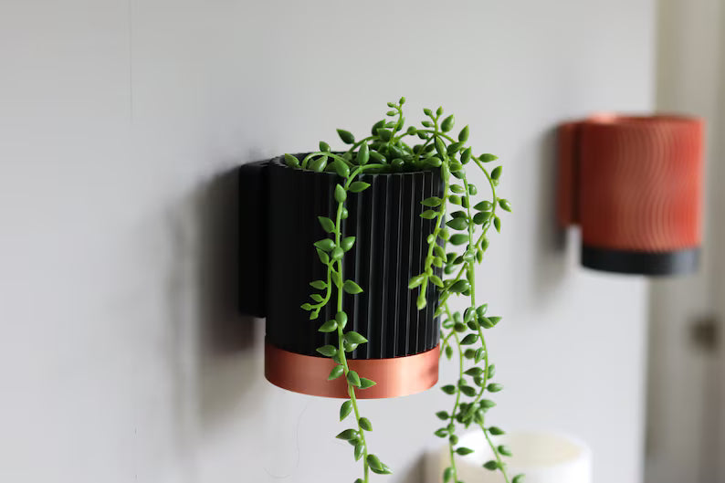 Vasi da parete bicolore nero e rame con piante decorative su muro chiaro