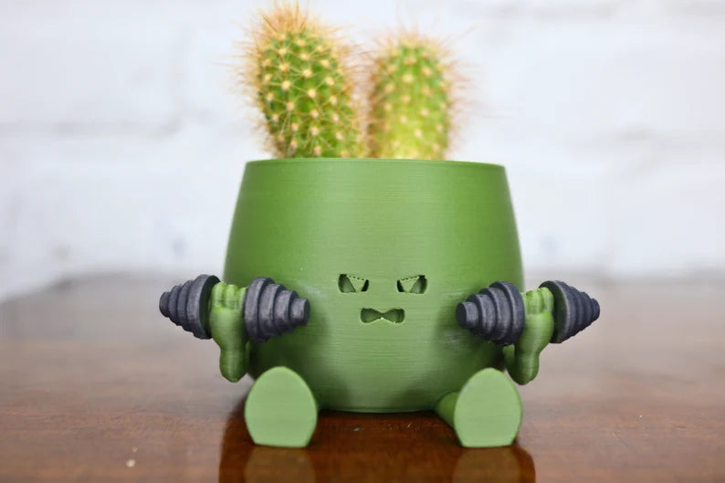 Vaso a forma di personaggio verde con manubri e cactus sulla testa