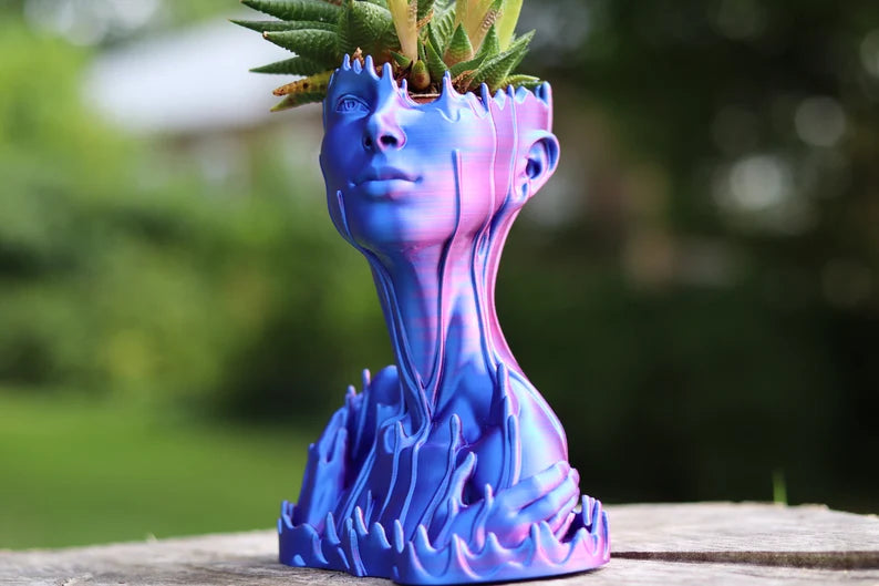 Vaso artistico blu e viola a forma di volto umano con pianta sulla testa