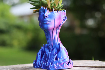 Vaso artistico blu e viola a forma di volto umano con pianta sulla testa