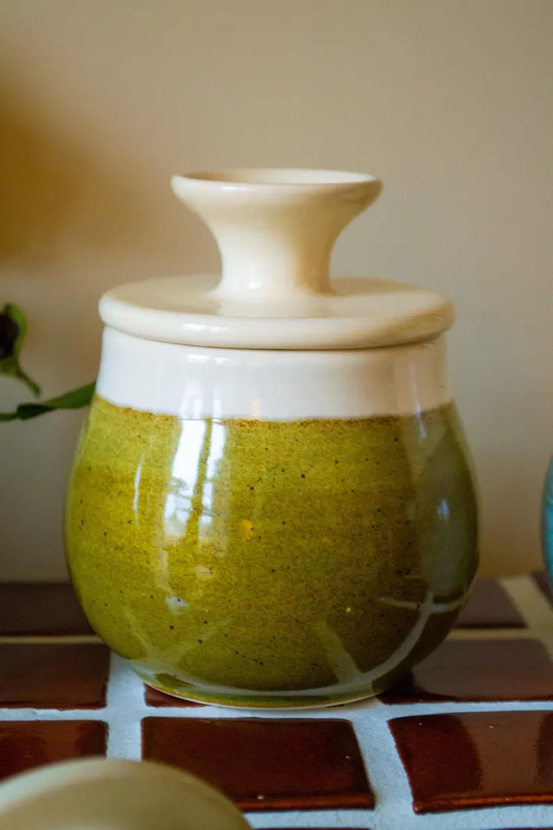 Vaso in ceramica smaltata verde con coperchio decorativo su superficie piastrellata