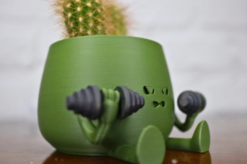 Vaso verde a forma di personaggio che solleva manubri con cactus piantato sopra